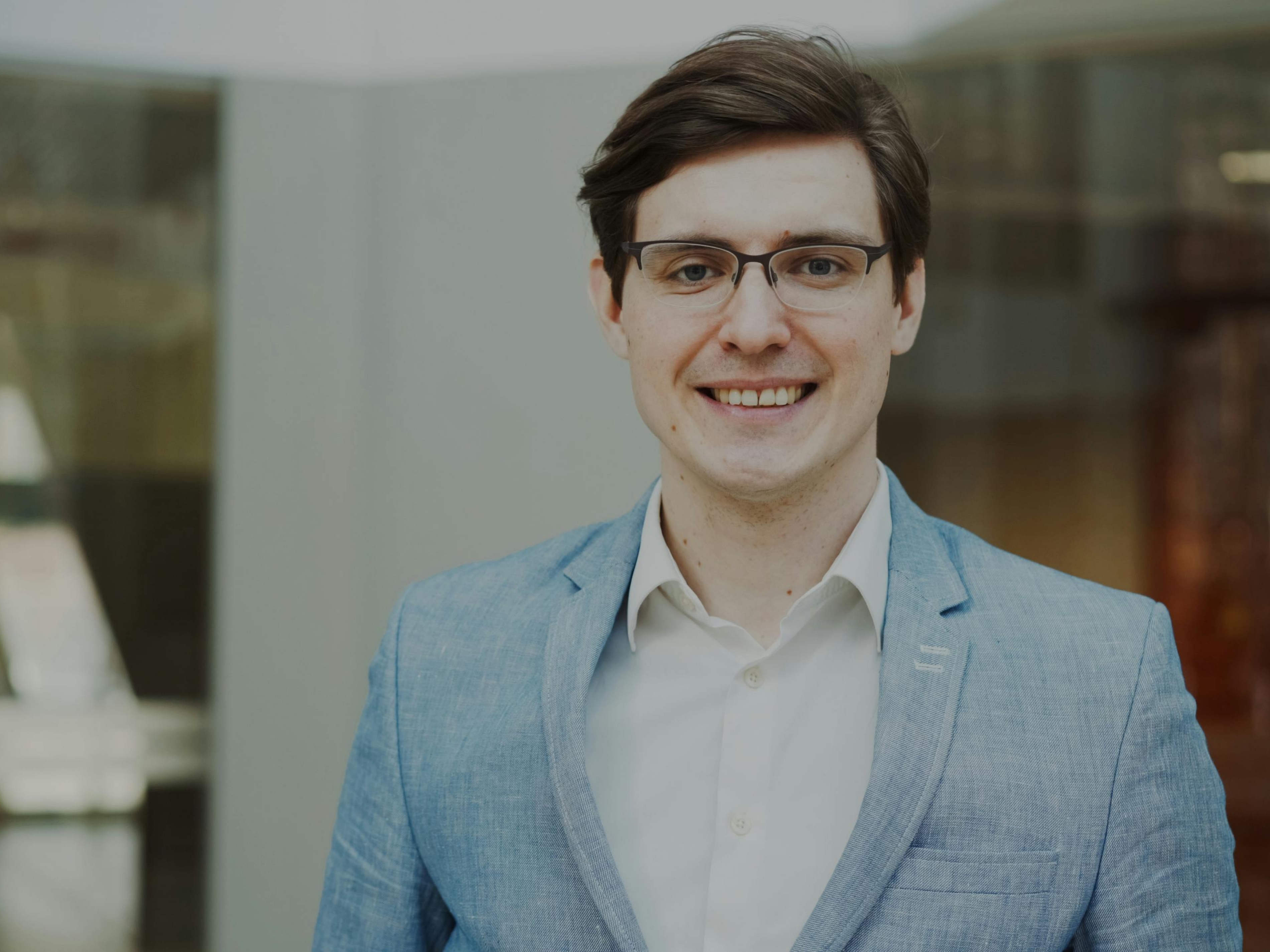 Nivel Gurung poses, smiling, at the camera, while standing on the UBalt campus outside its Academic Center.
