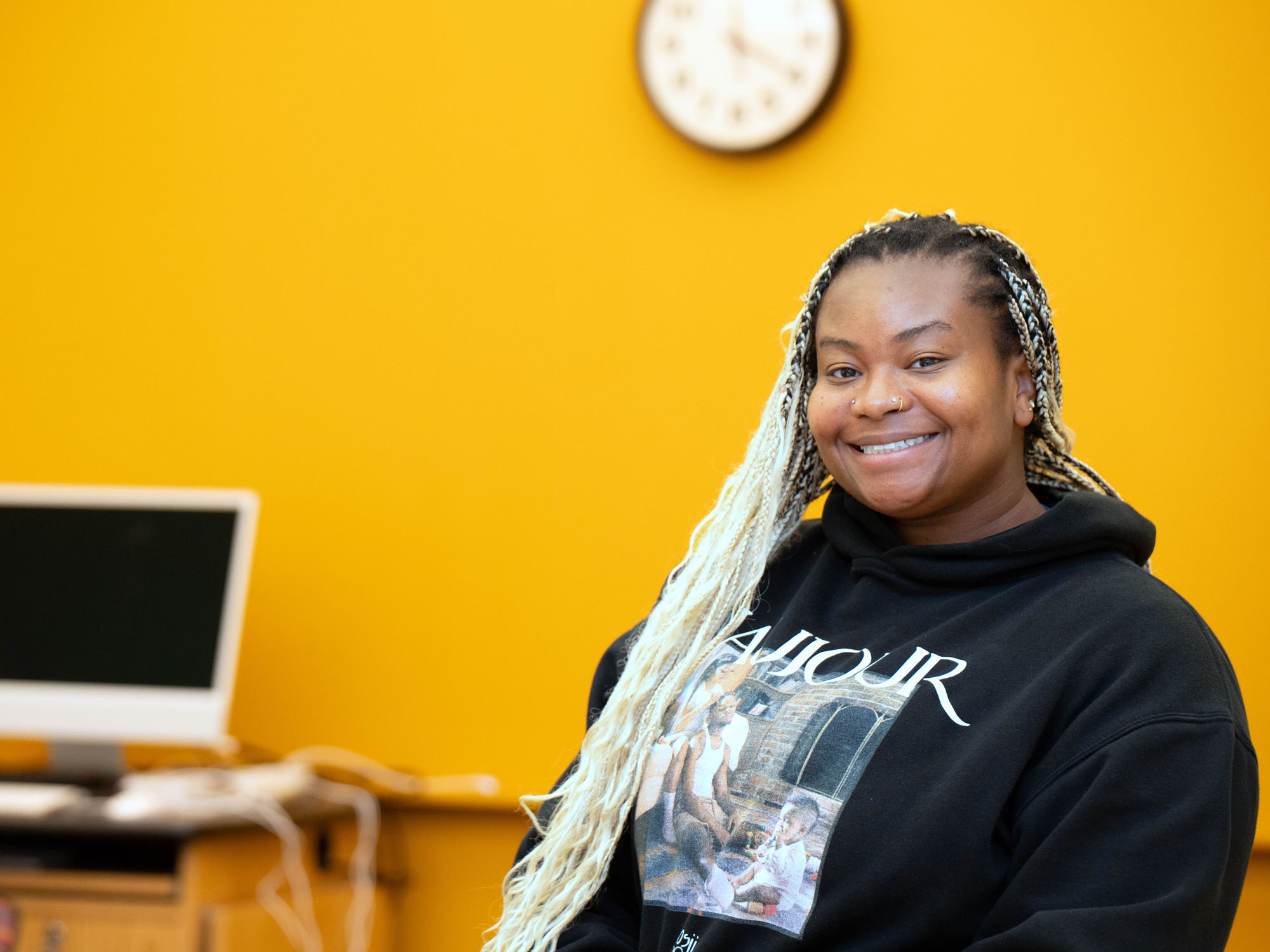 Student Nes Agopome smiles at the camera while sitting in a yellow-walled classroom.